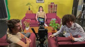 Three actors sit accross from each other, looking at the director on symmetrically balanced set.